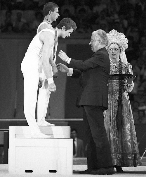 Девушка в народном костюме держит поднос с олимпийскими медалями. СССР 1980 г.